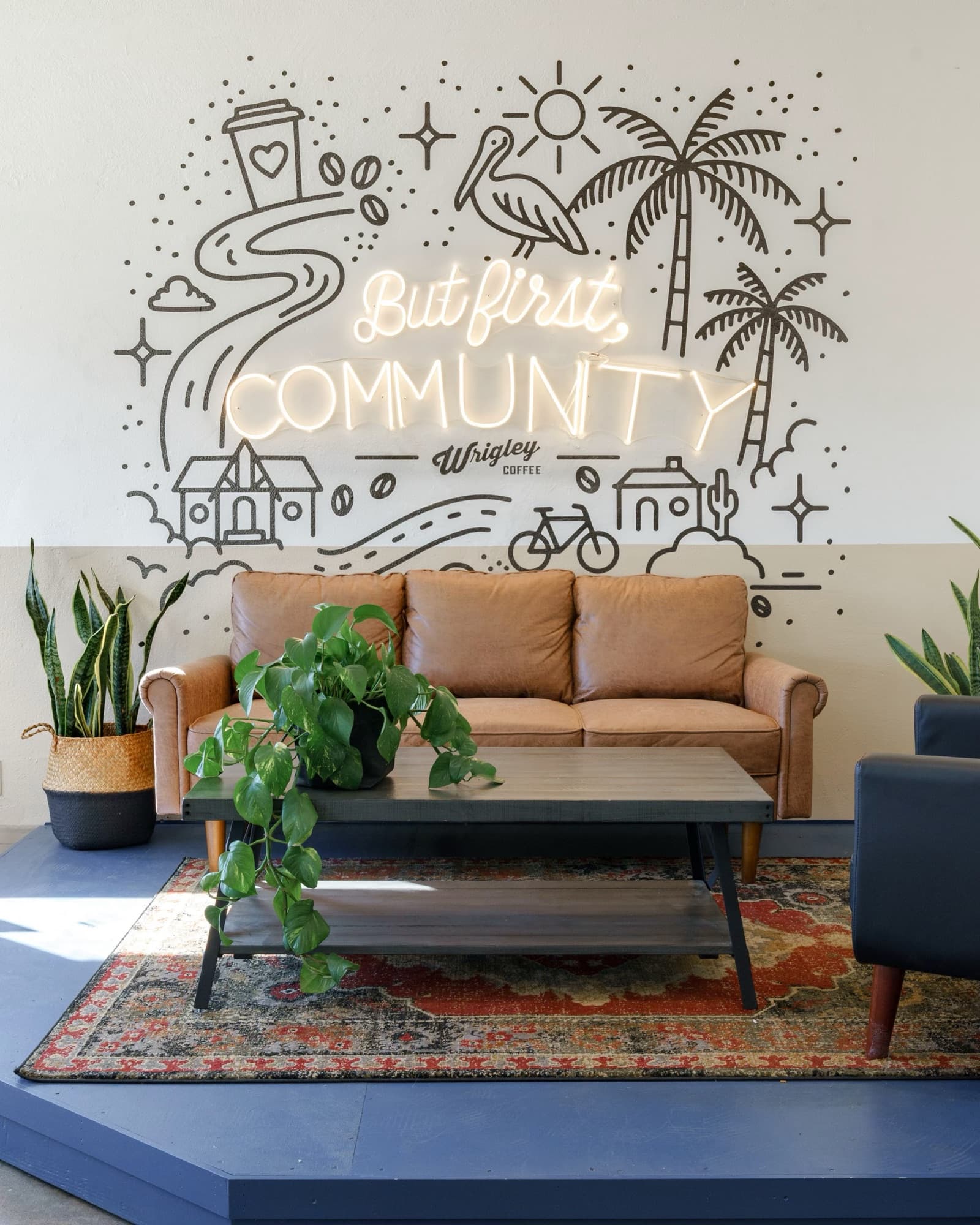 A leather couch under a wall mural that reads But first, Community