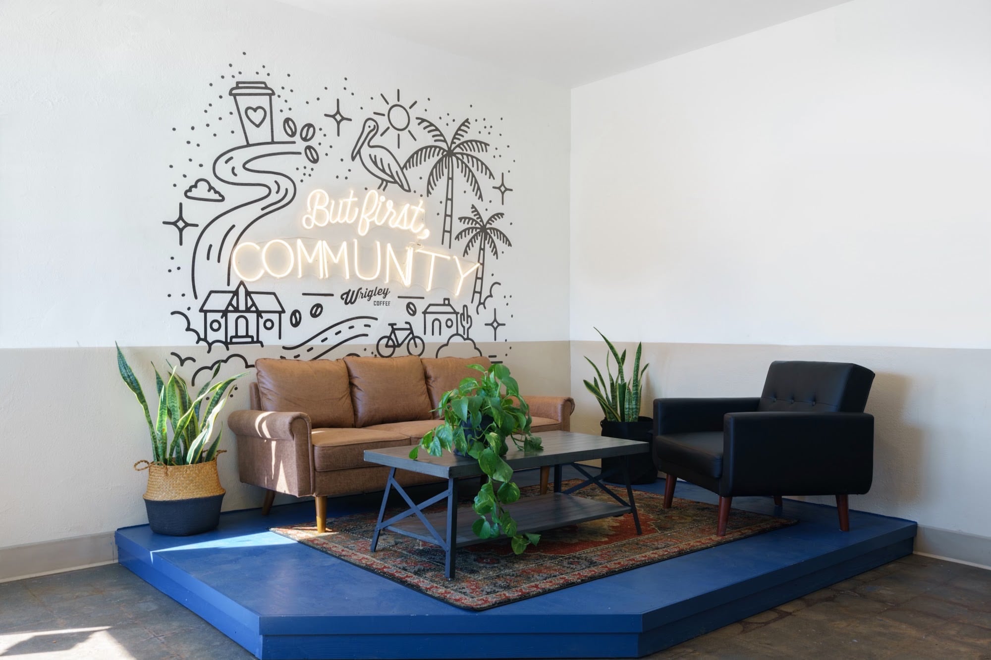 A lounge at Wrigley Coffee with a wall mural that reads But first, Community