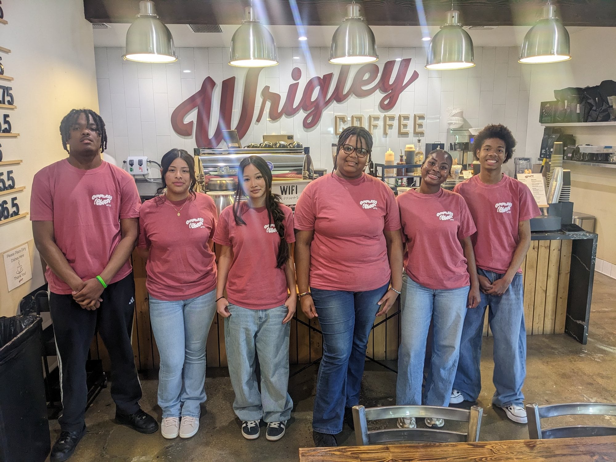 Six spring 2026 pilot grads in red shirts stand together in front of the Wrigley Coffee counter