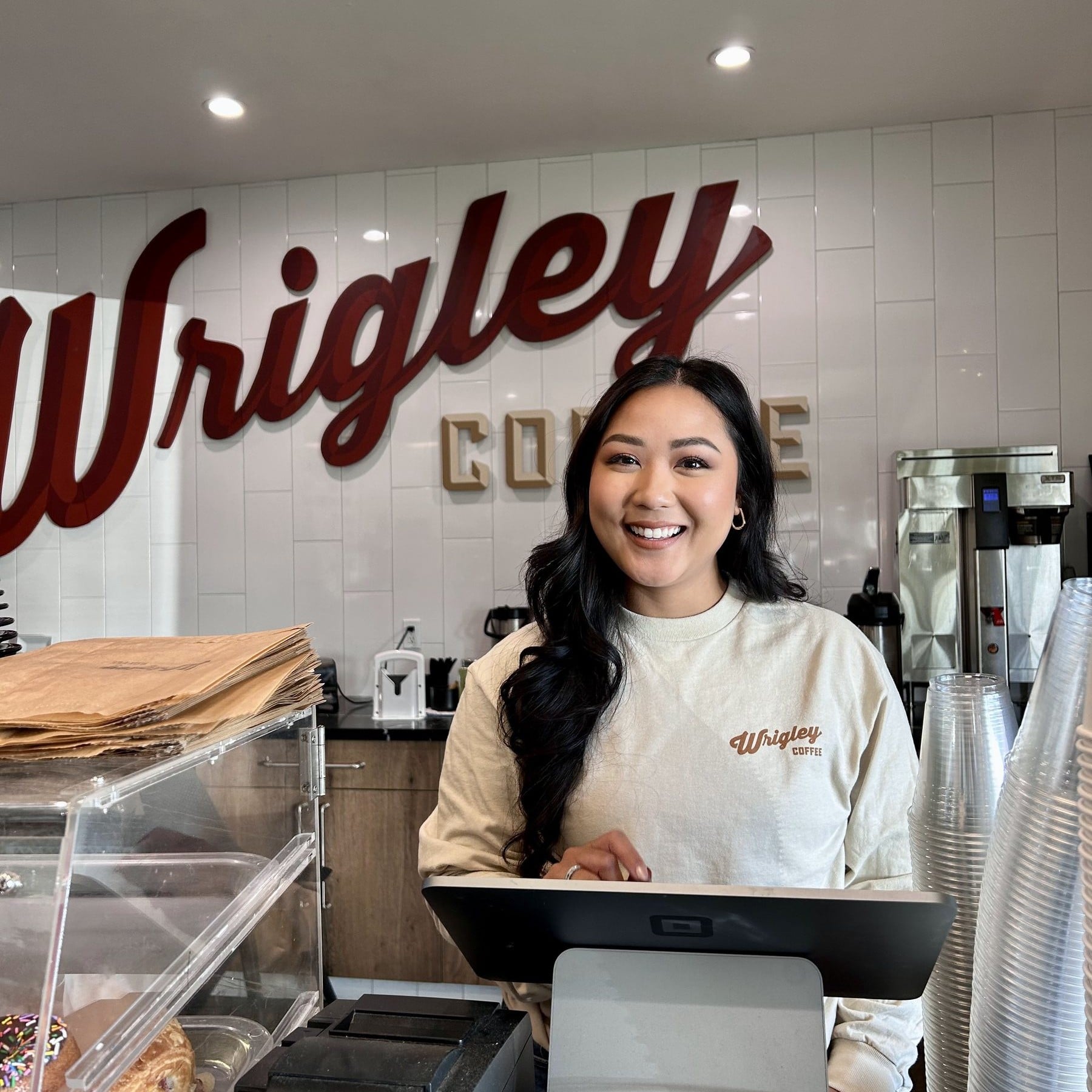 A smiling Wrigley Coffee team member at the register under the Wrigley Coffee sign